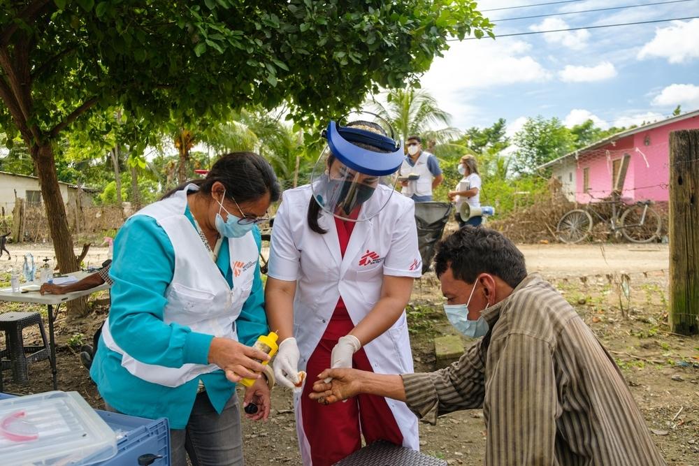 MSF staff in surgical masks disinfect the finger of a person wearing a surgical mask.
