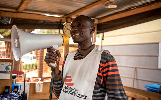 An MSF staff holds a white megaphone to their face.