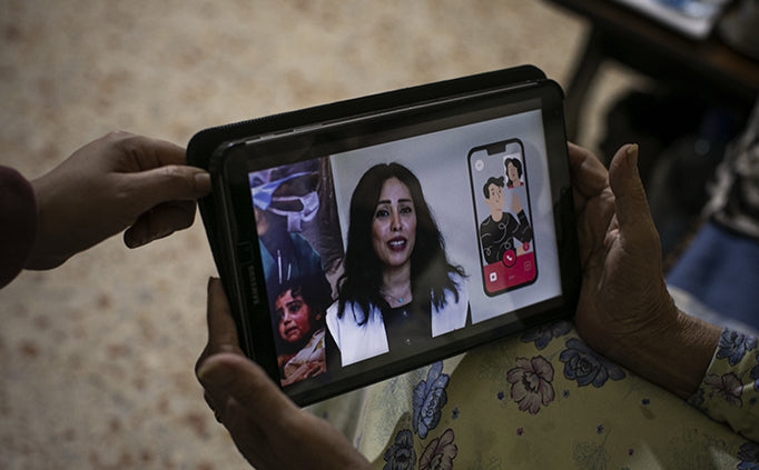 Hands holding a computer tablet with a person on the screen.