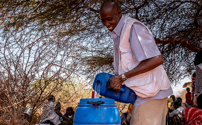 An MSF staff pours water into a blue barrel.