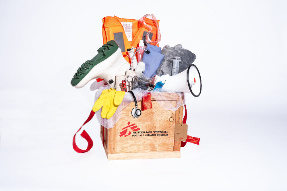 A wooden crate overflows with items including a stethoscope, a lifejacket, surgeon's tools, a blanket, thermometer, megaphone and rubber boots.