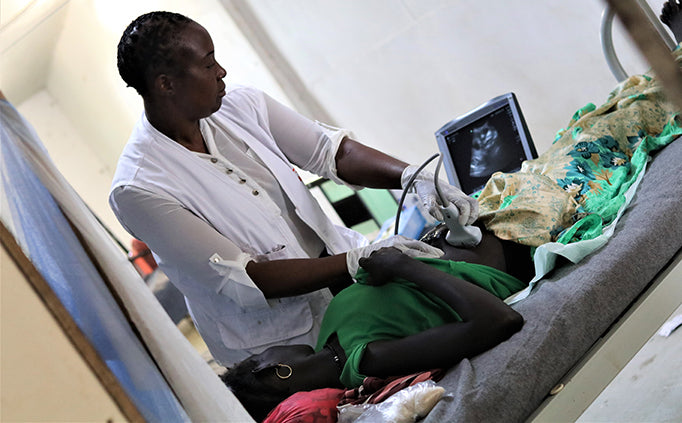 A healthcare worker watches an ultrasound monitor while moving a medical device over a patient's stomach.
