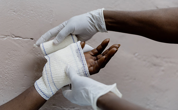 Close up of two hands in medical gloves wrapping medical dressings around another person's wrist and hand. 