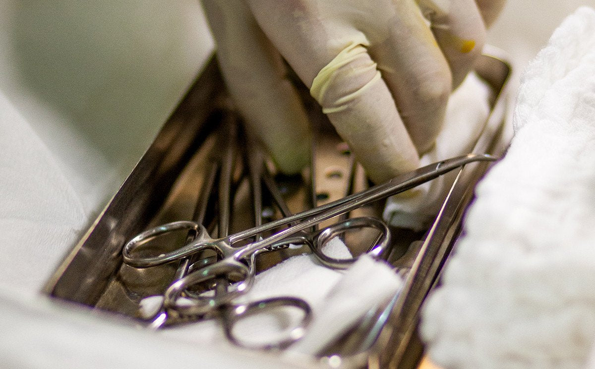 A gloved hand reaches for a set of surgical instruments.