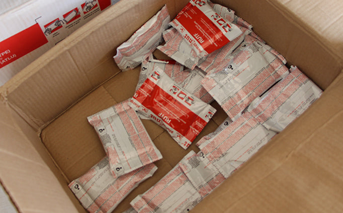 An open cardboard box filled with red and white packets of therapeutic food.