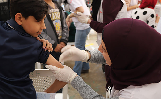 A nurse holds the upper arm of a child in preparation for a vaccination. 