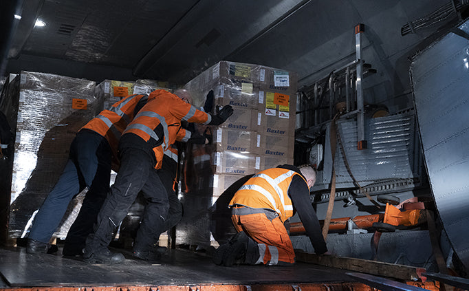 Three people move a skid of boxes inside a delivery truck.