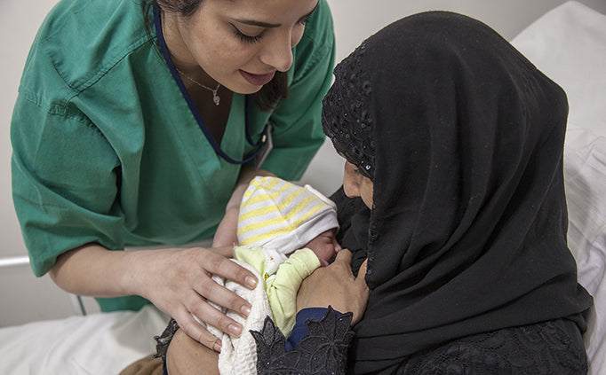 A medical staff passes a newborn baby to their mother.