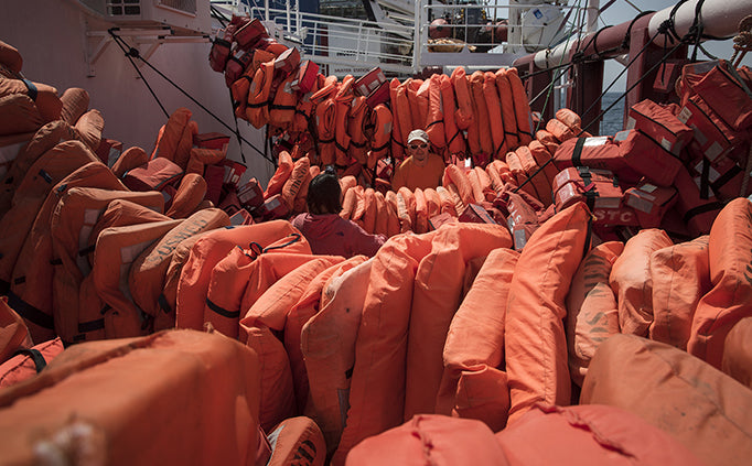 Dozens of orange life jackets hang over a series of ropes.