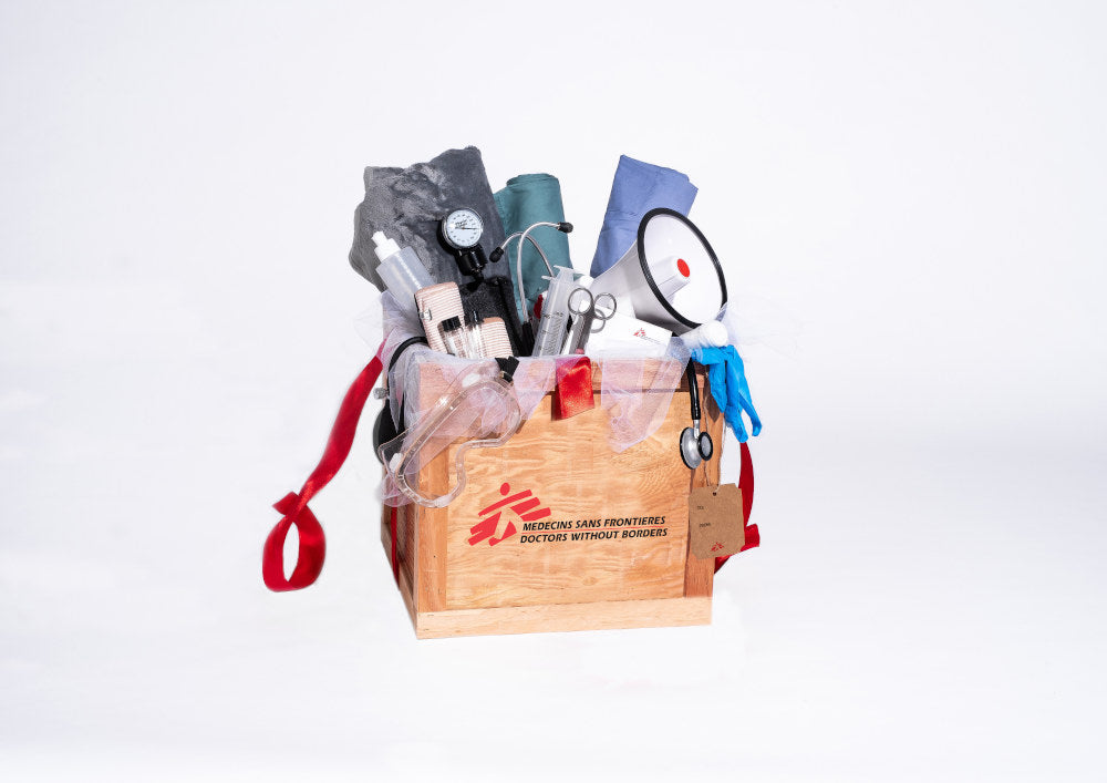 A wooden crate overflows with items including a stethoscope, a lifejacket, surgeon's tools, a blanket, thermometer, megaphone and rubber boots.