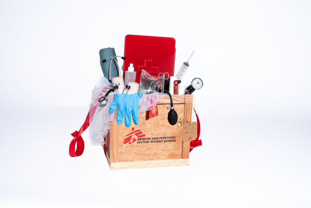 A wooden crate overflows with items including a stethoscope, a lifejacket, surgeon's tools, a blanket, thermometer, megaphone and rubber boots.
